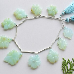 May include: A strand of light blue opal flower beads with silver connectors and blue tassels. The beads are carved in a flower shape and are strung on a silver chain.