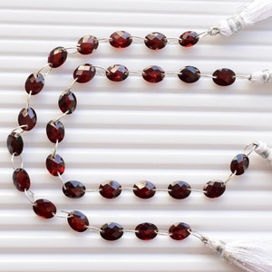 May include: A strand of red gemstone beads with silver connectors and white tassels at each end.