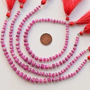 May include: Four strands of pink ruby gemstone beads with faceted surfaces, each strand is strung with silver wire and finished with a red tassel.