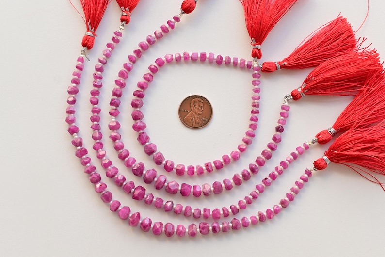 以下が含まれることがあります： ファセットカットされたピンクのルビーのビーズが4本、それぞれシルバーワイヤーで糸に通され、赤いタッセルで仕上げられています。