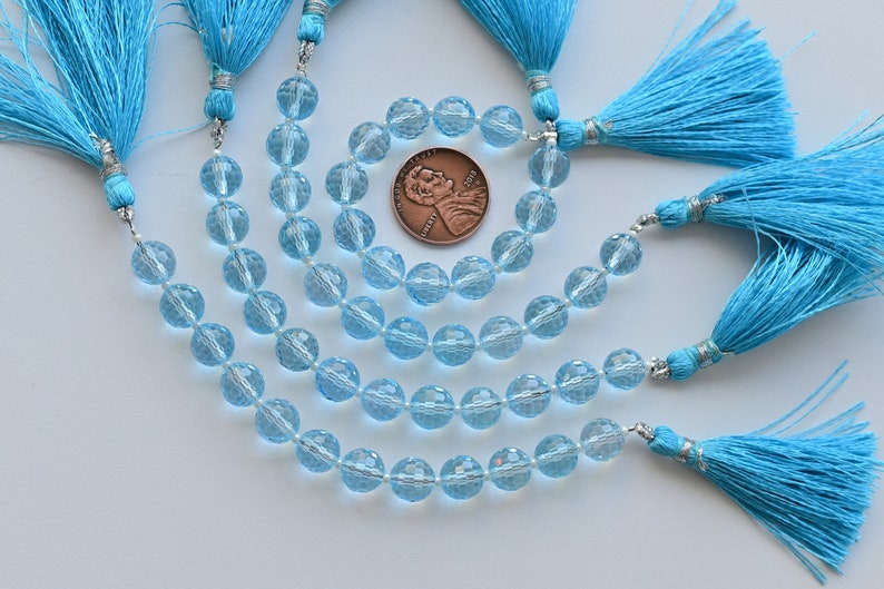 Puede incluir: Una hebra de cuentas de piedras preciosas facetadas de color azul claro con borlas plateadas. Las cuentas son redondas y tienen un acabado facetado. Las borlas est&aacute;n hechas de un material suave y esponjoso. Las cuentas tienen aproximadamente 8 mm de di&aacute;metro.