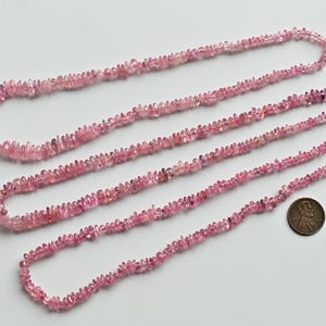 Könnte beinhalten: Vier Stränge rosa Turmalinperlen, jede Strähne ist etwa 46 cm lang. Die Perlen sind klein und unregelmäßig geformt und ähneln winzigen Chips. Ein US-Penny ist zur Größenbestimmung enthalten.