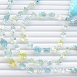 May include: Three strands of gemstone beads in shades of blue and yellow, with blue tassels at each end. The beads are strung on silver wire.
