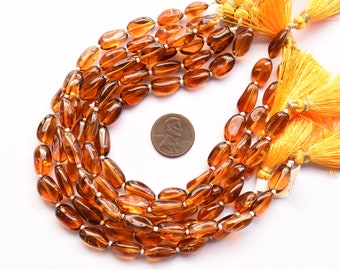May include: A strand of brown oval-shaped gemstone beads with a gold tassel. The beads are approximately the size of a US penny.