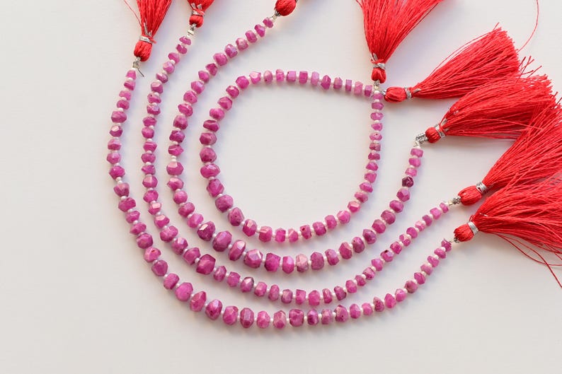 以下が含まれることがあります： 銀色の留め具と赤いタッセルが付いた、ピンクの宝石ビーズの4連ネックレス