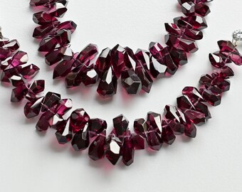 May include: Three strands of dark red gemstone beads, each strand is made of faceted, irregular shaped beads. The beads are strung on a clear cord.
