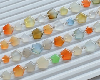May include: A strand of gemstone beads in various colors, including orange, yellow, green, blue, and white. The beads are connected by silver jump rings and are arranged in rows on a white surface.