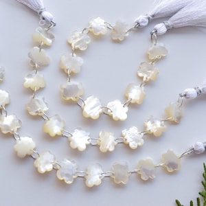 May include: Strands of flower-shaped beads in a creamy white hue, strung together with silver-colored wire. Each strand is finished with a white tassel. The beads have a subtle iridescent sheen.