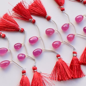May include: A set of pink gemstone beads with silver connectors and red tassels. The beads are oval shaped and the tassels are made of a soft, fluffy material.