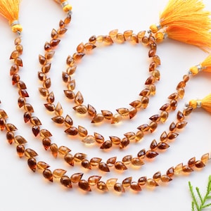 May include: A set of four strands of brown gemstone beads with a teardrop shape. Each strand has a yellow tassel at the end.