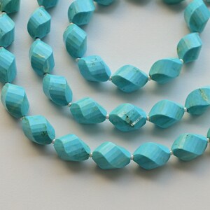 May include: A strand of turquoise gemstone beads, each bead is faceted and has a unique shape. The beads are strung on a silver wire and have a tassel at the end.