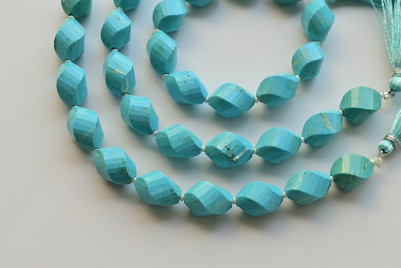 May include: A strand of turquoise gemstone beads, each bead is faceted and has a unique shape. The beads are strung on a silver wire and have a tassel at the end.