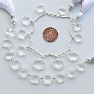 May include: A strand of clear crystal flower beads strung on silver wire with white tassels at each end. The beads are approximately the size of a US penny.