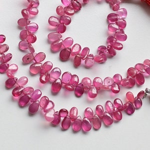 May include: A strand of pink gemstone beads, with a teardrop shape, strung on a silver cord with tassels at each end.