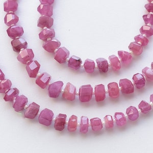 May include: A strand of pink gemstone beads, with faceted, square-shaped beads. The beads are strung on a clear thread.