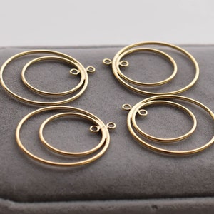 May include: Four gold-toned double hoop earrings with a circular design. The earrings are on a gray surface.