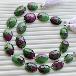 May include: A strand of green and pink oval-shaped gemstone beads with silver connectors and white tassels at each end.