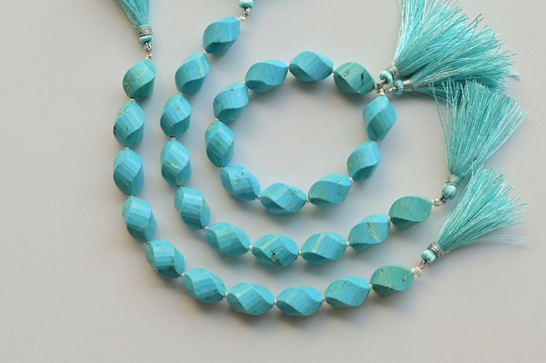 May include: Three strands of turquoise beads with a faceted, oval shape. Each strand has a turquoise tassel at the end.