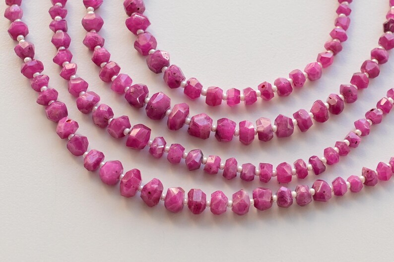 以下が含まれることがあります： 白い糸に、ファセットカットされたピンクのルビービーズが連なっています。ビーズは重ねて配置され、繊細でエレガントな外観になっています。