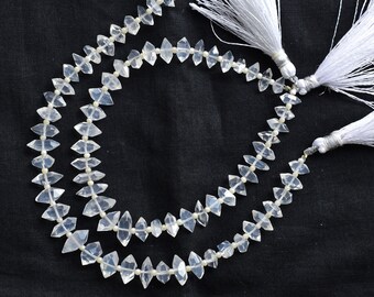 May include: Two strands of clear quartz crystal beads with faceted, diamond-like shapes. The beads are strung on a white cord with small, round spacers. White tassels are attached at the ends, against a black background.