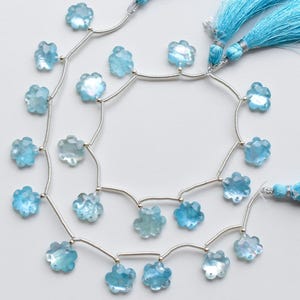May include: Strands of light blue, flower-shaped beads strung on silver wire, with matching blue tassel accents. The beads are faceted, catching the light. Ideal for jewelry making.