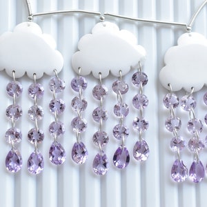 Könnte beinhalten: Ein weißer, wolkenförmiger Anhänger mit einer silbernen Kette und mehreren Strängen aus Amethyst-Edelsteinen, die daran hängen. Der Anhänger ist Teil einer Halskette mit mehreren Wolken und Amethyst-Strängen.