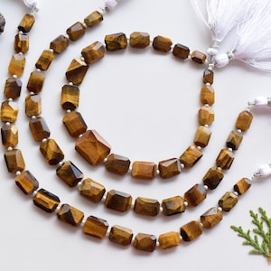 May include: Three strands of faceted tiger's eye beads in shades of brown and gold. The beads are strung on a cord with white tassels at the ends.