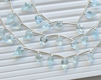 May include: A strand of light blue aquamarine gemstone beads strung on silver wire. The beads are faceted and have a teardrop shape.
