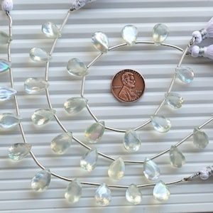 May include: A strand of iridescent white teardrop-shaped gemstone beads strung on silver wire. The beads are approximately the size of a US penny.