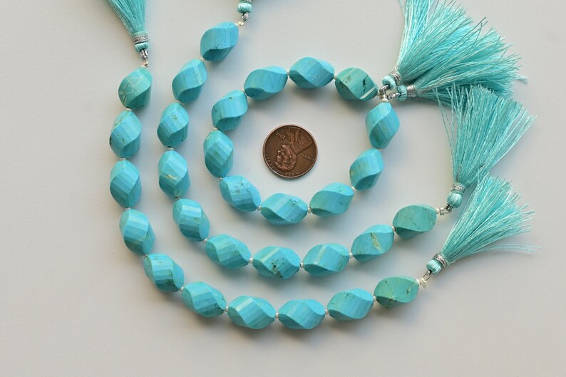 May include: Three strands of turquoise beads with a faceted, twisted design. The beads are a vibrant blue-green colour and are strung on a silver cord. Each strand has a turquoise tassel at the end.