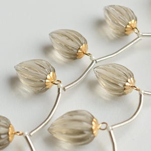 Puede incluir: Un collar de cadena de plata con múltiples hebras presenta una serie de cuentas transparentes, facetadas, en forma de lágrima con acentos dorados.