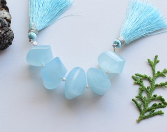 May include: A strand of light blue gemstone beads with silver accents and blue tassels on each end.