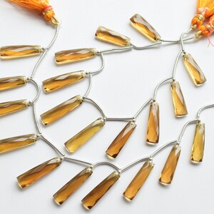 May include: A strand of faceted, golden brown gemstone beads with silver connectors and orange tassels at each end.
