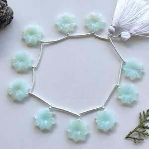 May include: A strand of light blue opal flower beads with silver connectors. The beads are strung on a silver chain with a white tassel at the end.