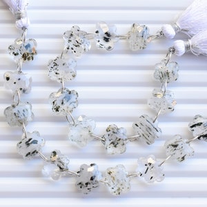 May include: A strand of white and black gemstone beads with a flower shape. The beads are strung on silver wire and have a white tassel on each end.
