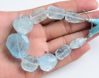 May include: A strand of light blue aquamarine gemstone beads with a light blue tassel. The beads are faceted and have a natural, irregular shape.
