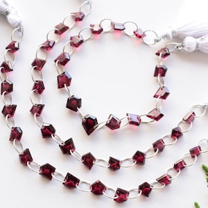 May include: Three strands of a red gemstone necklace with silver chain links and white tassels on each end.