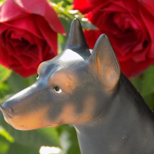 May include: A black and brown ceramic dog figurine with a textured surface. The figurine is positioned in front of a red rose.