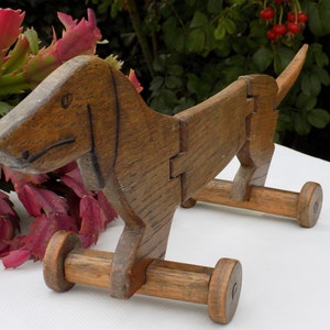 Può includere: Un giocattolo di legno a forma di bassotto con dettagli dipinti di marrone e quattro ruote. Il giocattolo è fatto di legno naturale e ha un design semplice e rustico.