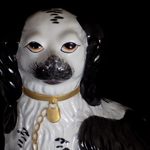 K&ouml;nnte beinhalten: Eine schwarz-wei&szlig;e Porzellanfigur eines Hundes mit goldenen Akzenten. Der Hund tr&auml;gt ein goldenes Halsband und eine Kette mit einem goldenen Schloss. Die Augen des Hundes sind orangefarben bemalt.