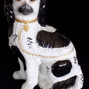 K&ouml;nnte beinhalten: Eine schwarz-wei&szlig;e Porzellanfigur eines Hundes mit einem goldenen Kettenhalsband. Der Hund sitzt mit leicht geneigtem Kopf. Die Figur ist handbemalt mit aufwendigen Details.