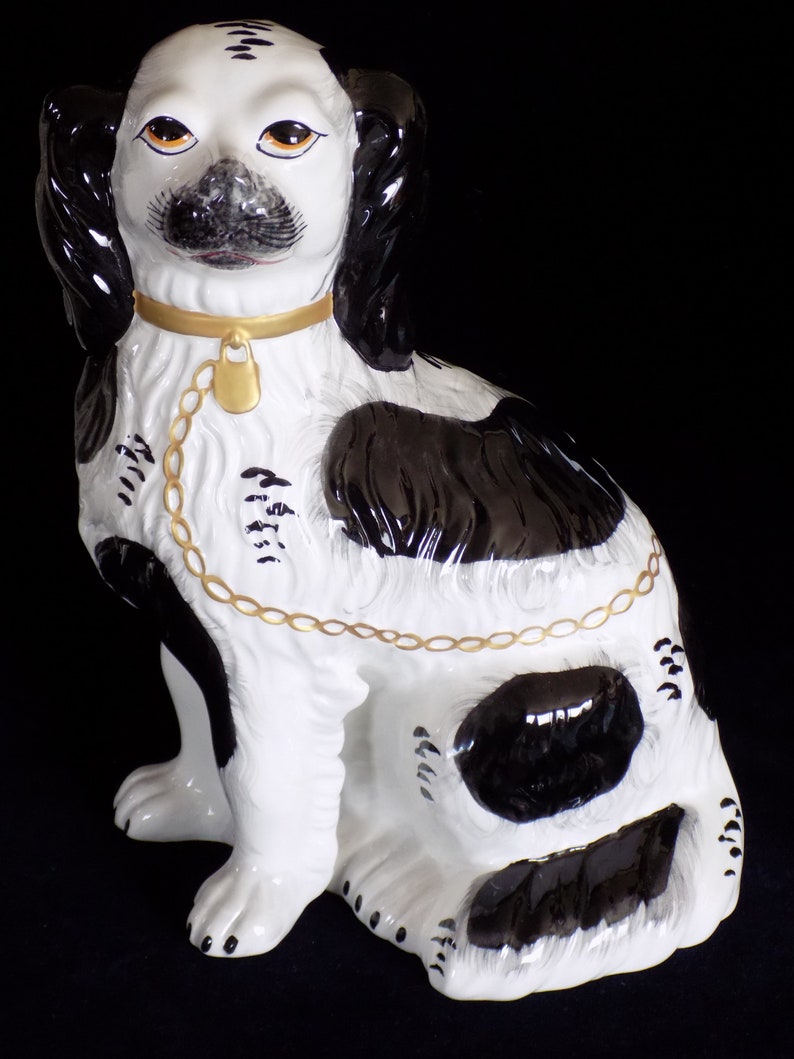K&ouml;nnte beinhalten: Eine schwarz-wei&szlig;e Porzellanfigur eines Hundes mit einem goldenen Kettenhalsband. Der Hund sitzt mit leicht geneigtem Kopf. Die Figur ist handbemalt mit aufwendigen Details.