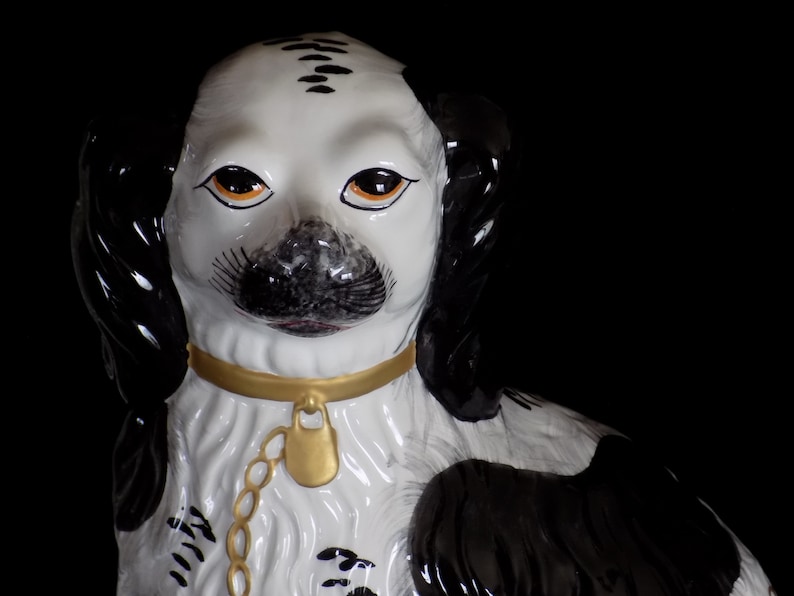 K&ouml;nnte beinhalten: Eine schwarz-wei&szlig;e Porzellanfigur eines Hundes mit goldenen Akzenten. Der Hund tr&auml;gt ein goldenes Halsband und eine Kette mit einem goldenen Schloss. Die Augen des Hundes sind orangefarben bemalt.
