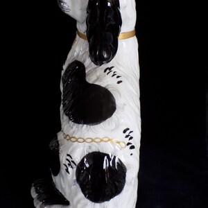 K&ouml;nnte beinhalten: Eine schwarze und wei&szlig;e Keramik-Hundefigur mit goldenen Akzenten. Der Hund sitzt aufrecht mit dem Kopf zur Seite geneigt. Er hat schwarze Flecken auf seinem wei&szlig;en K&ouml;rper und einen schwarzen Schwanz.
