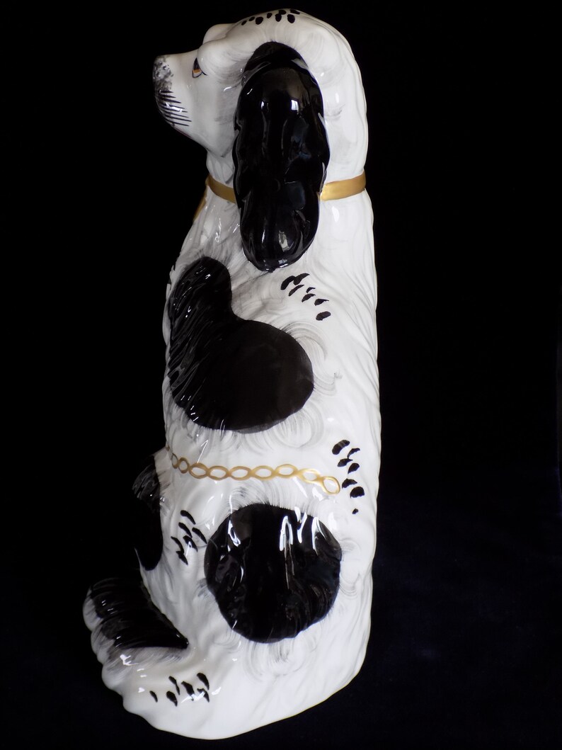 K&ouml;nnte beinhalten: Eine schwarze und wei&szlig;e Keramik-Hundefigur mit goldenen Akzenten. Der Hund sitzt aufrecht mit dem Kopf zur Seite geneigt. Er hat schwarze Flecken auf seinem wei&szlig;en K&ouml;rper und einen schwarzen Schwanz.