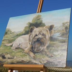 May include: A painting on canvas of a brown and white Yorkshire Terrier dog lying down in a grassy field. The dog is looking at the viewer with its tongue slightly sticking out. The background is a green field with a small stream and trees in the distance.
