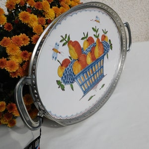 May include: A white oval serving tray with a silver rim and handles. The tray features a hand-painted design of a blue basket filled with oranges, pears, and grapes. Two butterflies are also painted on the tray.