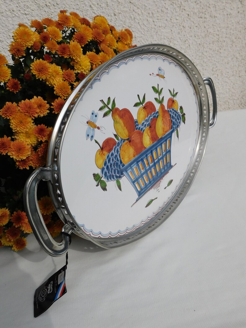 May include: A white oval serving tray with a silver rim and handles. The tray features a hand-painted design of a blue basket filled with oranges, pears, and grapes. Two butterflies are also painted on the tray.