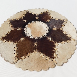 Peut inclure: Un tapis rond en patchwork multicolores en cuir de vache. Le tapis est cousu avec un fil brun clair et a un bord festonné.