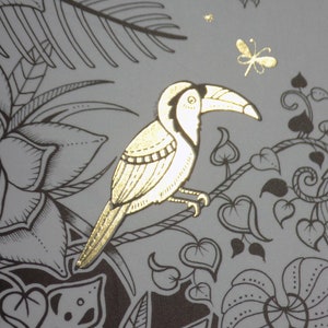 K&ouml;nnte beinhalten: Ein goldener Tukan mit langem Schnabel sitzt auf einem Ast mit schwarzen und wei&szlig;en Bl&auml;ttern. Der Tukan ist von einem floralen Design mit einer Libelle im Hintergrund umgeben.